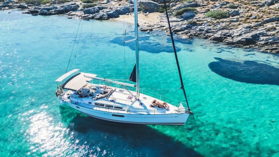 A white sloop anchored over sand in clear water off Dia Island, Crete